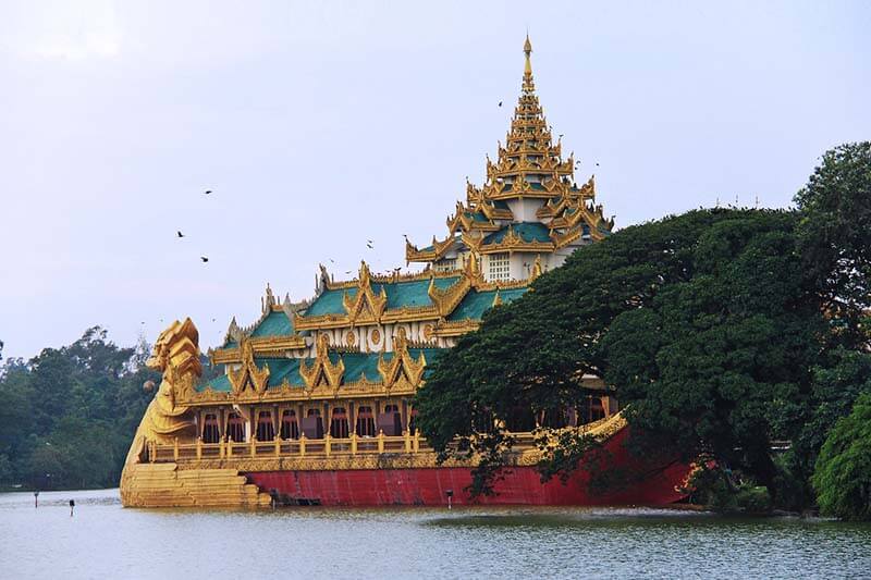 El sereno Parque Kandawgyi con el majestuoso Palacio Karaweik reflejado en las tranquilas aguas del lago